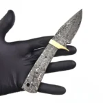 Raindrop-pattern knife blank with guard in gold tone, exposed full tang, two small holes, and a larger rear opening beside an inch-and-centimeter ruler