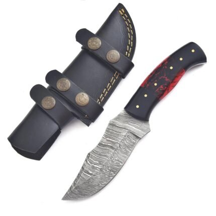 Red and black fixed blade knife with a silver-grey patterned blade and six gold-tone pins beside a black sheath with yellow stitching and decorative fittings.