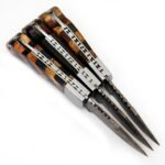 Three Damascus-Pattern Folding Knives with brown chevron, dark wood-grain and blue geometric handles, displayed beneath three embossed tan-brown knife sheaths.