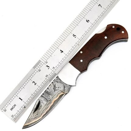 Damascus Pattern Skinner Knife with curved silver-gray blade, brown wood-grain handle, finger grooves and decorative fittings beside an inch-marked ruler.