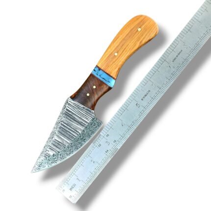 Damascus Pattern Mini Skinning Knife with curved silver-gray blade, two-tone brown wood-grain handle, turquoise-blue spacer and gold-colored pins beside a metal ruler.